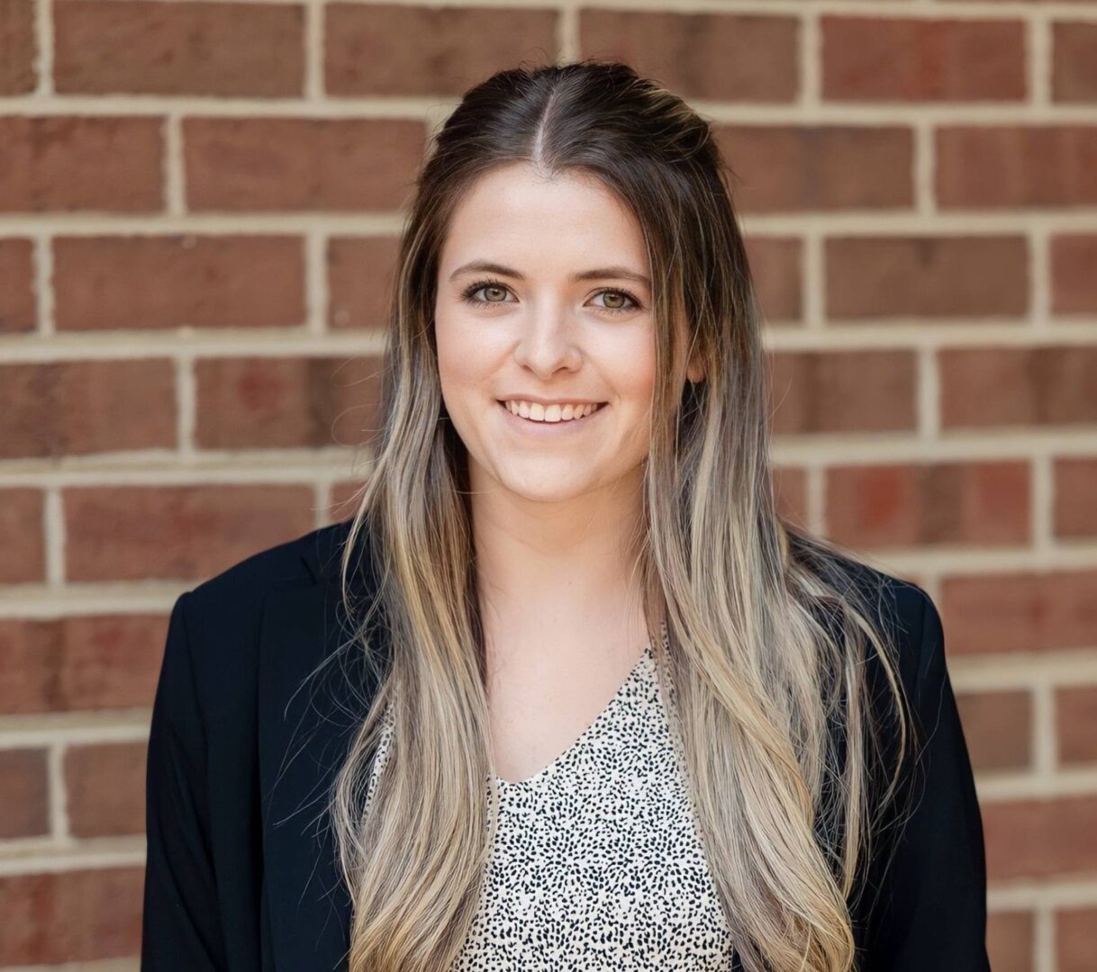 A woman with long hair standing in front of a brick wall.